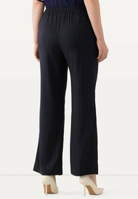 Marinblå randiga vida byxor med elastiskt midjeband. Tyget verkar slätt och kompletteras av beige högklackade skor nertill.