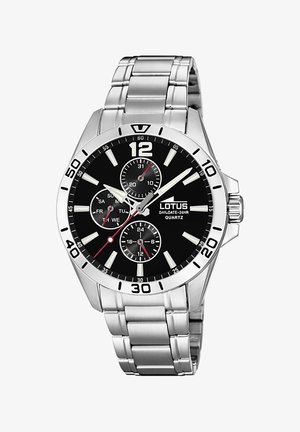 Srebrna ura iz nerjavnega jekla z črnima dialom, belimi oznakami ur, rdečimi poudarki in več poddialom za dan in datum. Kvartni mehanski sistem.