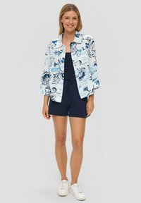 Chemise à boutons florale avec des motifs bleus et navy sur fond blanc, associée à une combinaison navy et des baskets blanches.