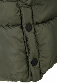 Podrobnost z olivno zeleno napihnjeno jakno, ki prikazuje kviltano teksturo, okrogle črne gumbe in šive, ki obkrožajo blazine.