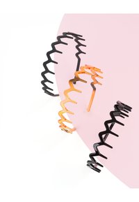 Drie haaraccessoires met zigzagpatroon—zwart, oranje en metallic—gemaakt van glad plastic op een roze achtergrond.