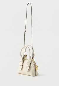 Mini bolsa em couro creme com alças superiores duplas, alça de ombro ajustável, ferragens douradas, fecho de zíper e tachas decorativas.