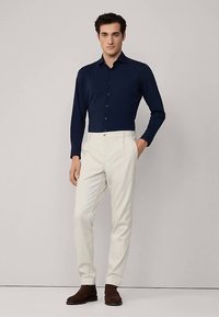 Marinblå långärmad skjorta med knappar, ihop med krämfärgade byxor. Bruna skor kompletterar outfiten med en enkel, stilren design.