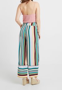 Striped wide-leg pants with multicolored vertical stripes, featuring a soft fabric, cuffed hems, and a high waistband. Paired with a fitted pink top.