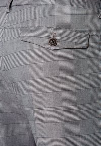 Szare i czarne spodnie w kratkę z zapięciem na guzik w tylnej kieszeni, o teksturowanym wykończeniu i gładkiej tkaninie ogólnie.