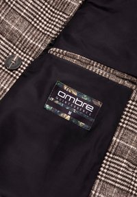 Ruskea ja kerma houndstooth-kuvioinen takakangas mustalla sisätaskulla, jossa on "Ombre Quintessence" -logo.