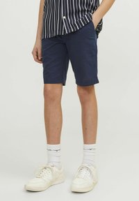 Shorts bleu marine en coton, dotés d'un devant plat et de poches latérales, associés à des chaussures blanches et à une chemise rayée.