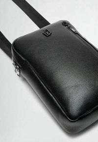 Borsa a tracolla in pelle nera con superficie texturizzata, dotata di zip superiore, tracolla regolabile e un logo goffrato discreto.