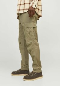 Khaki cargo broeken met meerdere zijzakken, taps toelopende boorden en een duurzame katoenmengselstof, gecombineerd met bruine veterschoenen.