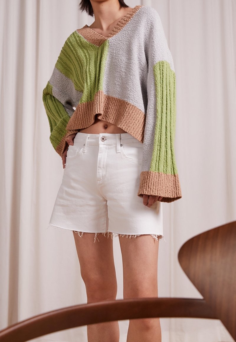 Gebreide trui met groene en grijze strepen, een bruine zoom en losse mouwen; gecombineerd met witte denim shorts met rafelige randen.