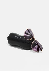 Ochelari de soare aviator din metal cu lentile degradate de culoare violet închis, accente aurii și o husă neagră cu fermoar inscripționată "vogue."