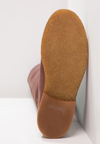 Brun läderstövel med en textured yta och en platt gummisula. Sulan har en något upphöjd kant och prentat varumärke.