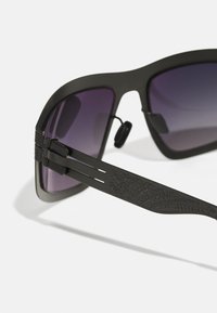 Black sunglasses with a matte finish and gradient purple lenses. Features a textured arm with detailed pattern and adjustable nose pads.