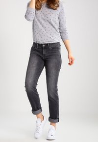 Vaqueros de mezclilla gris con un ajuste holgado y bajos remangados, combinados con una camisa de manga larga gris claro con un sutil patrón de anclas.