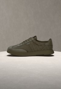 Καθημερινό sneaker χαμηλό σε ελιά πράσινο με κορδόνια εμπρός, επένδυση στον γιακά και επίπεδη ελαστική σόλα, παρουσιασμένο σε ουδέτερο φόντο.