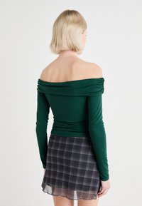 Grønn av-shoulder topp med langermet, med innsamlede stoffdetaljer og en tettsittende silhuett, parret med et svart rutete miniskjørt.
