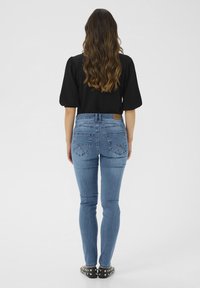 Modré úzké džíny s vysokým pasem a pěti kapsami. Na zadní straně se nachází dekorativní prošití a hnědá kožená nášivka. Černý top a boty se cvočky.