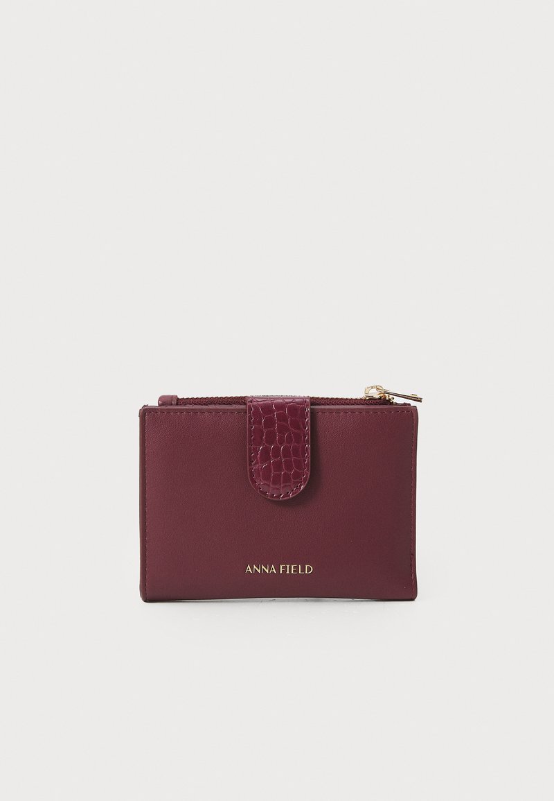 Burgundy nahka-lompakko, jossa on tekstuurinen krokotiilikuosiset flap, kultainen vetoketju ja kohokuvioitu "ANNA FIELD" -logo alareunassa.