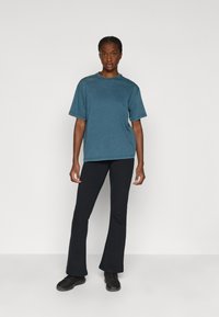 Tengeri kék pamut póló kerek nyakkal, rövid ujjakkal és laza szabással, fekete harangnadrággal és fekete sportcipővel párosítva.