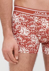 Boxer da uomo a fantasia floreale rossa con una texture morbida, caratterizzati da un cinturino bianco a contrasto con dettagli del marchio.