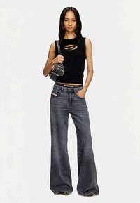 Juodas rankovių marškinėlis su išpjovomis, pilki plačiomis kojomis džinsai ir blizgi juoda peties rankinė. Ant džinsų matomas prekės ženklo ženklinimas.