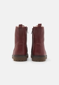 Botas de cuero burdeos hasta el tobillo con cierre de cremallera, acentos de costura y suela de goma texturizada. La vista trasera muestra un detalle de talón reforzado.