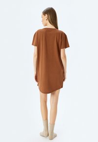 Vestido camiseta de gran tamaño en color marrón con mangas cortas, dobladillo curvado y textura suave, combinado con calcetas beige claro hasta la rodilla.
