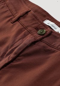 Hnědé látkové kalhoty s knoflíkovým zapínáním, zipem a štítkem na pase. Materiál má hladký, mírně lesklý povrch.