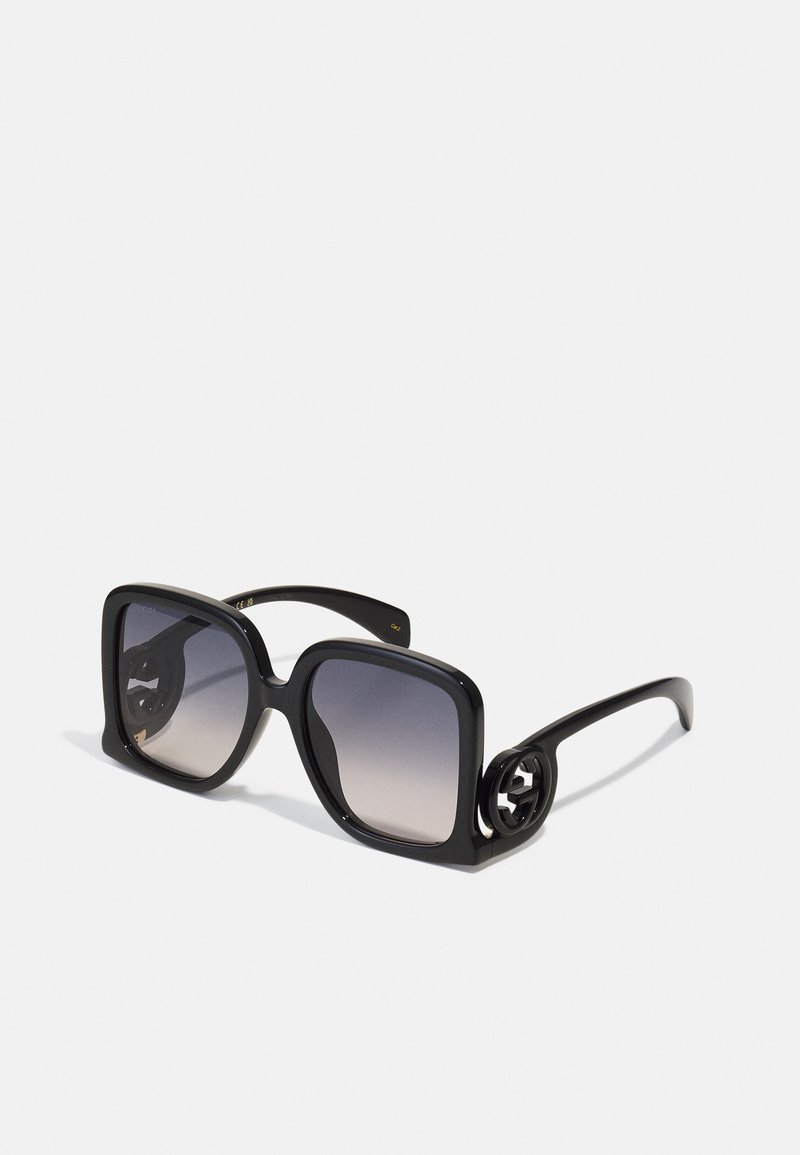 Gafas de sol negras de gran tamaño con lentes degradados. Montura rectangular gruesa, acabado brillante y acento de logo en el lateral.