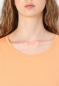 Peachfarget t-skjorte med rund hals og korte ermer, laget av glatt stoff, med et enkelt design og minimale sømdetaljer.