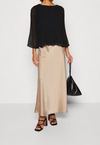 Schwarze Faltenbluse, beiger satinmaxikleid, schwarze Sandalen mit Blockabsatz und eine schwarze Lederhandtasche. Glatte Texturen und fließendes Design.