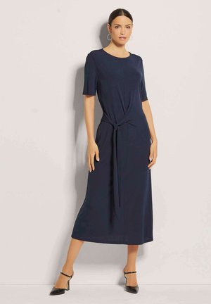 Marineblaues knielanges Kleid mit kurzen Ärmeln, Knotenoptik an der Taille, glatte Stofftextur, runder Ausschnitt, kombiniert mit schwarzen High Heels.