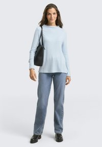 Helles blaues, geripptes Langarmoberteil, kombiniert mit blauen Jeans und schwarzen Stiefeletten. Eine schwarze Schultertasche sorgt für einen Kontrast. Einfaches Design, strukturiertes Oberteil.
