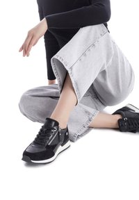 Zapatillas negras que combinan cuero y ante, con suela blanca, detalle de cremallera en el costado y puntera redondeada. Llevadas con pantalones grises de pierna ancha.