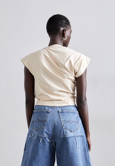 Un tricou bej scurt, cu mâneci tip capac, asortat cu blugi largi de culoare albastru decolorat, având margini desfăcute și buzunare din spate înclinate.