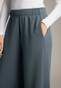 Tyrkysové rebrované nohavice s širokými nohavicami, elastickým pásom a bočnými vreckami, predstavajúce textúrovanú látku v uvoľnenom strihu.