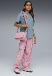 Lyseblå T-shirt med rynket pink strop, lys pink cargo-bukser, pink crossbody taske og pink sneakers med grå såler.