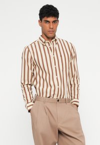 Ilgi piedurkņu pogāmata krekls ar krēmkrāsas un brūnas vertikālas svītras dizainu, ar kabatu un zīmola logo uz krūšu daļas.