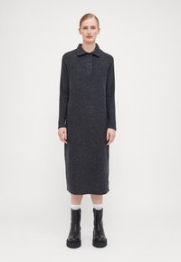 Rochie tricotată lungă, de culoare gri închis, cu guler și trei nasturi. Modelul poartă cizme negre până la gleznă și șosete albe.