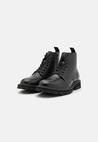 Zwarte leren enkelboots met vetersluiting aan de voorkant, zijrits en dikke rubberen zool met een robuust profiel. Glad textuur met minimale accenten.