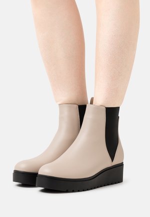 Bottes cheville en similicuir beige avec panneaux latéraux élastiques noirs et semelle plateforme noire texturée. Finition lisse, design à bout rond.
