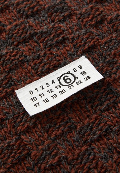 Tecido tricotado em vermelho escuro e cinza, com um padrão de espinha de peixe. Etiqueta anexada mostra o tamanho 6 com números impressos sobre um fundo branco.