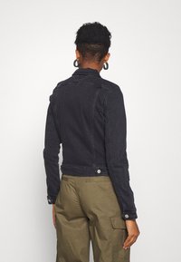 Dark denim jacket with a fitted design, featuring a collar, long sleeves, and snap buttons at the cuffs and hem. Back view shows minimalistic style.