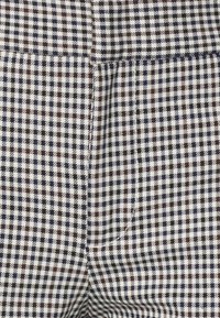 Károvaný materiál v bílé, námořnické modré a burgundské čtverce. Hladká textura, s upraveným střihem a viditelnými detaily šití.