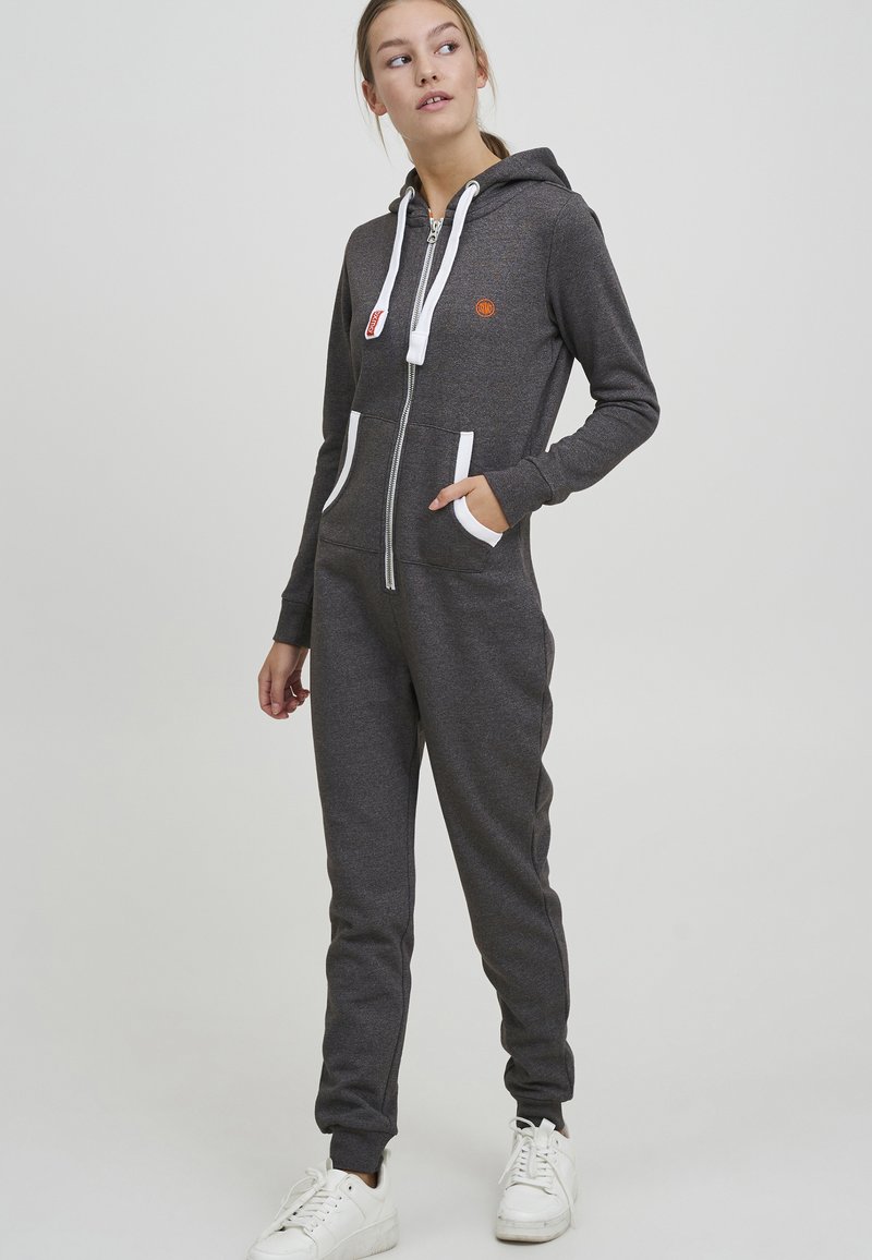 Šedý zip-up overálek s bílými detaily a kapsami; textura je hladká, vyrobený z měkké látky, s uvolněným střihem a kapucí se šňůrkou.