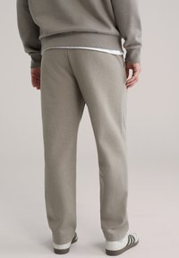 Lysegrå joggingbukser med løs pasform, blød tekstur, elastisk talje og sidelommer, parret med hvide og grønne sneakers.