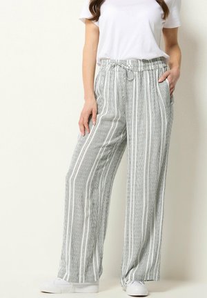 Donna che indossa pantaloni larghi a righe verticali grigie e bianche con vita elastica e sneakers bianche, abbinati a una maglietta bianca semplice.