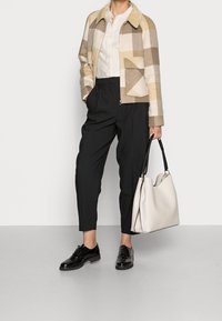 Villainen ruututakki beigen ja ruskean sävyissä, mustat housut, kiiltävät mustat kengät ja suuri valkoinen käsilaukku mustalla kahvalla.