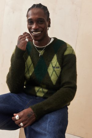 Groen en blauw ruitpatroon trui van fuzzy materiaal, gecombineerd met donkere jeans en zilveren sieraden. Lachend onderwerp dat zachtjes gebaart.