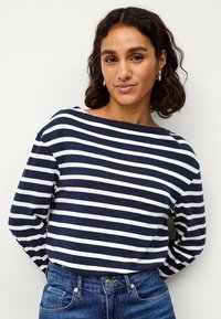 Marineblauwe en witte gestreepte top met lange mouwen en een bootnek, gecombineerd met blauwe denim jeans. De stof lijkt zacht met een comfortabele pasvorm.